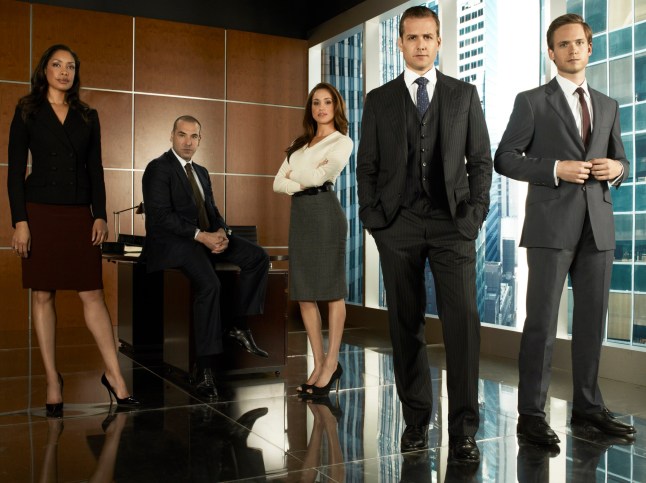 Suits stars Gina Torres as Jessica Pearson, Rick Hoffmann as Louis Litt, Meghan Markle as Rachel Zane, Gabriel Macht as Harvey Specter, Patrick Adams as Mike Ross in an office in a skyscraper