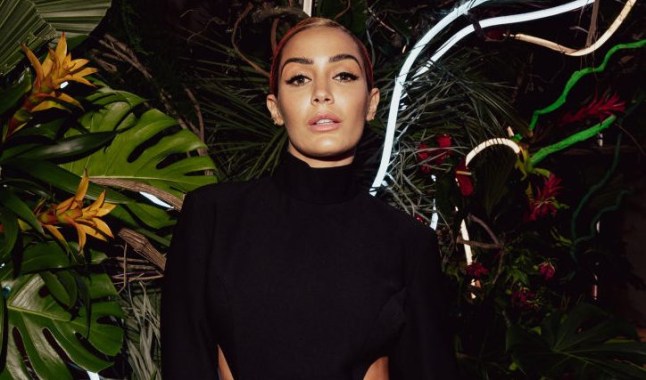 Frankie Bridge posing in front of a floral backdrop at the 2023 Baftas. She is wearing a black dress with cutouts on her sides