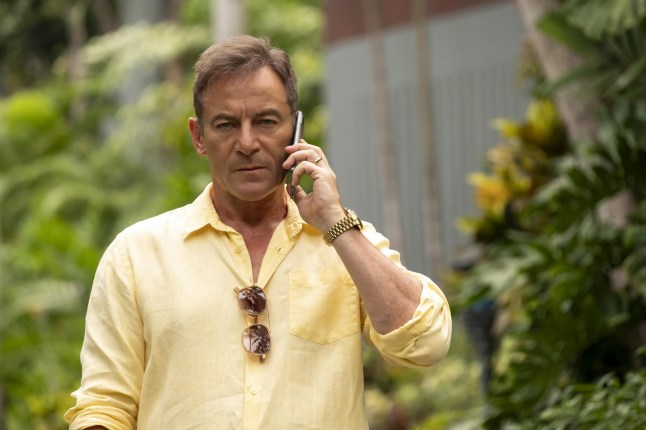 Jason Isaacs in the White Lotus. He's wearing a bright yellow shirt and speaking on the phone.