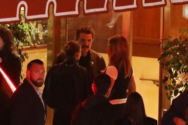 Jennifer Aniston and Pedro Pascal speaking to each other in a crown of people outside a restauran