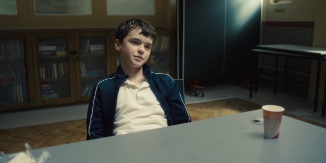 Owen Cooper as Jamie Miller in Adolescence. He's sitting at a table with a smug expression on his face.