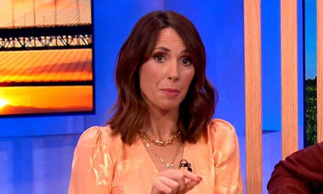 Alex Jones wearing an orange blouse and looking serious on The One Show