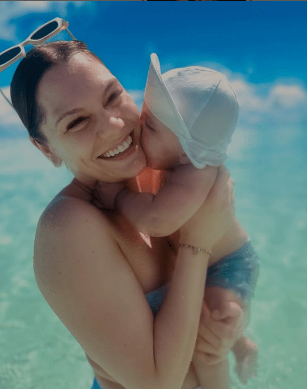 Jessie J stands in the ocean, beaming, holding her son Sky as a baby as he nibbles on her cheek