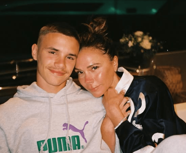 Victoria Beckham poses seated with her arm wrapped around her son Romeo, as they smile for the camera