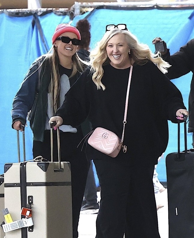 JoJo Siwa in a pink beanie, grey top and jacket, trousers and her mother, Jessalynn Siwa in an all-black outfit walking together with suitcases