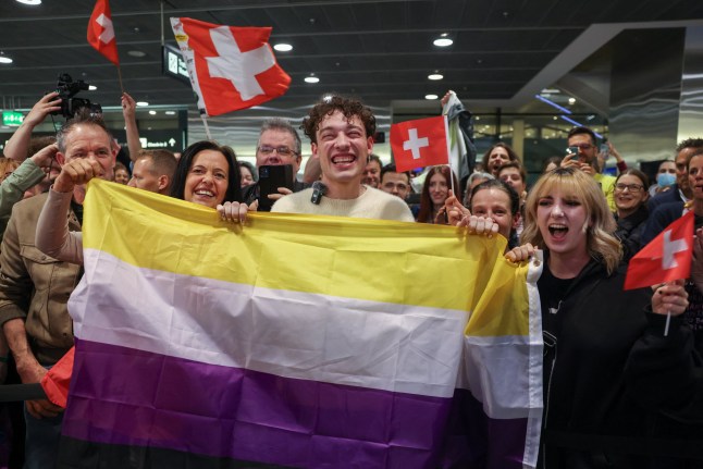 Nemo holding the non-binary flag with a crowd behind them holding up Swedish flags