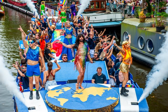 Conchita Wurst in a pride themed tassled outfit on a float with the world map with a crowd of people behind them holding pride flags