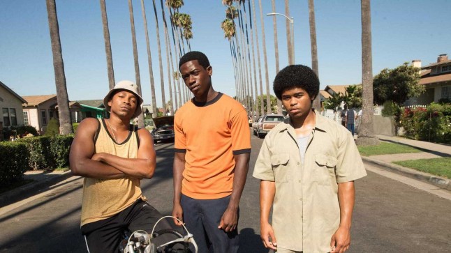 Damson Idris in Snowfall, standing next to two other men on a road flanked by palm trees.