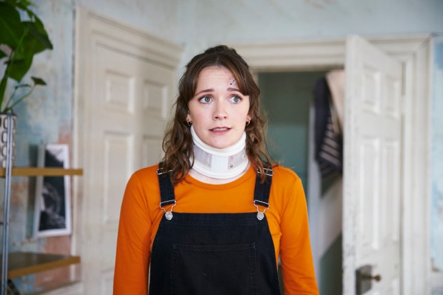 Charlotte Ritchie as Alison Cooper in Chosts wearing dungarees, an orange top and a neck brace