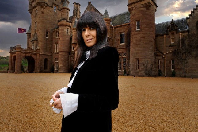 Claudia Winkleman in a black and white suit in front of the castle