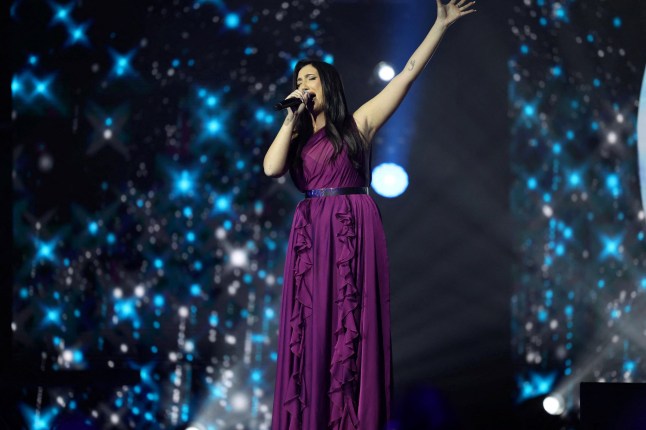 Israel's representative to the Eurovision Song Contest, Yuval Raphael, singing on stage in a long purple dress